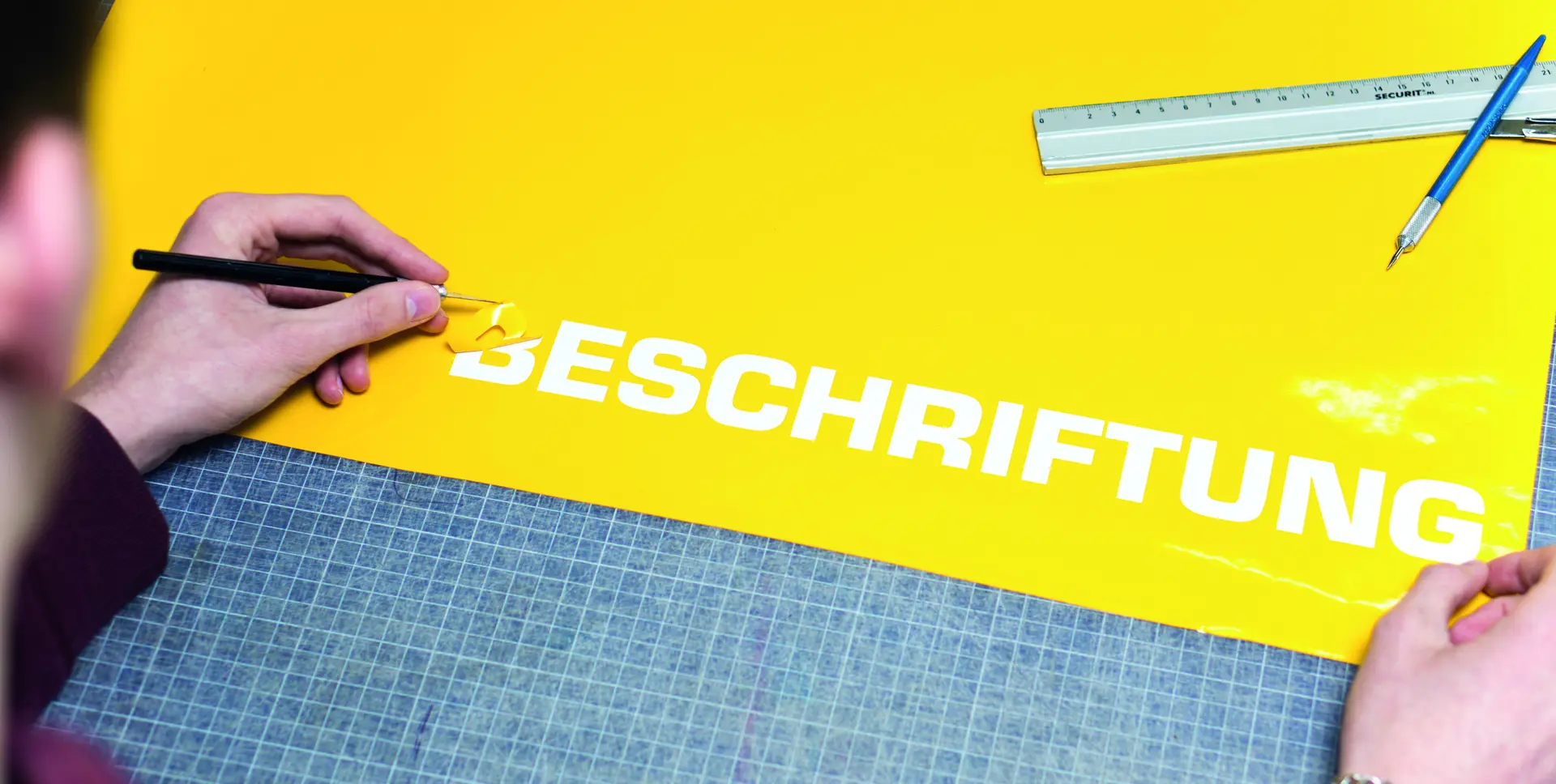 Werbetechnik Dümpel - Augsburg | Vinyl Schriftzug Basteln - BESCHRIFTUNG gelbes Blatt - Person Peeling - Metall Lineal Stift Schneidematte Arbeitsfläche.