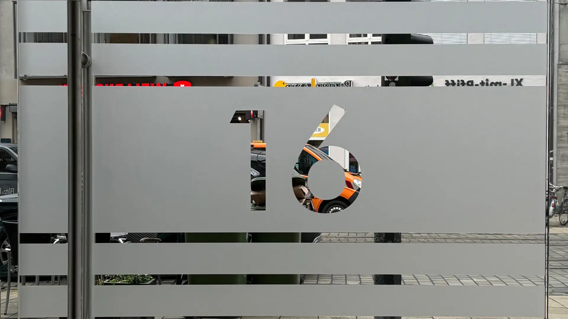 Werbetechnik Dümpel - Augsburg | Graues Metall-Lamellenpaneel - Ausschnitt der Nummer 16 - städtische Straßenansicht mit parkenden Autos - architektonisches Design - modernes Tor.