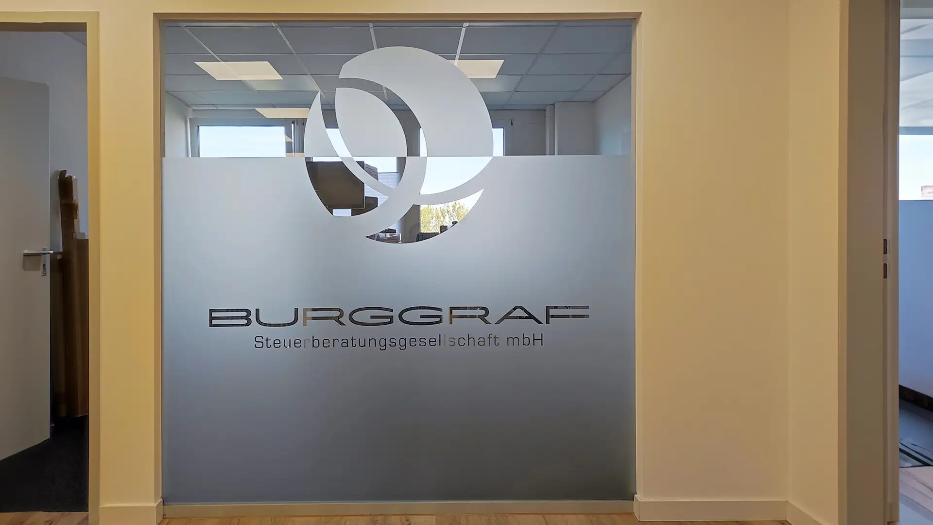 Werbetechnik Dümpel - Augsburg | BURGGRAF Steuerberatungsgesellschaft mbH Logo - Milchglas-Bürowand - schwarzer Schriftzug - moderne Steuerberatungseinrichtung sichtbar.