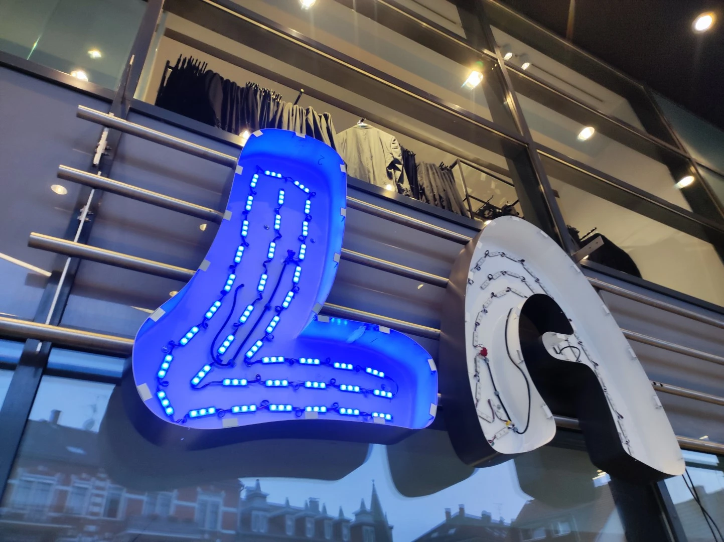 Werbetechnik Dümpel - Augsburg | Großes beleuchtetes LA-Schild mit freiliegender Verkabelung und LED-Leuchten an der Außenseite des Gebäudes - Kleiderständer sichtbar - Schaufenster in Los Angeles.