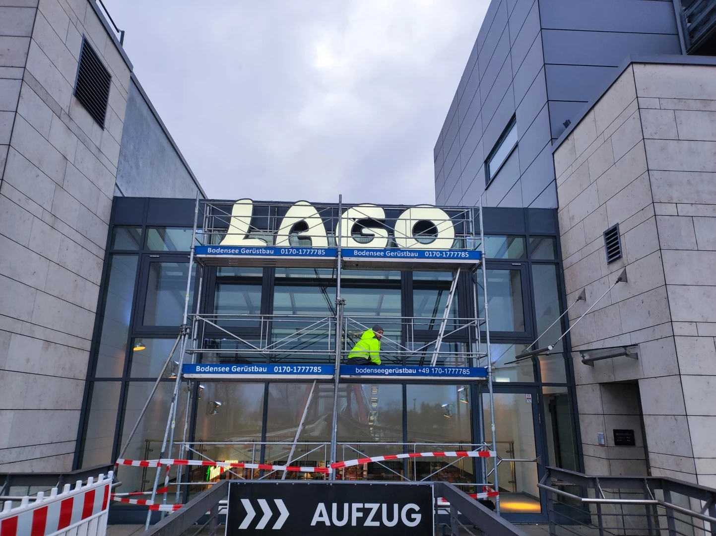 Werbetechnik Dümpel - Augsburg | Gebäudeeingangsgerüst - LAGO-Schild - Bauarbeiter in Warnweste - kommerzielles Renovierungsprojekt.