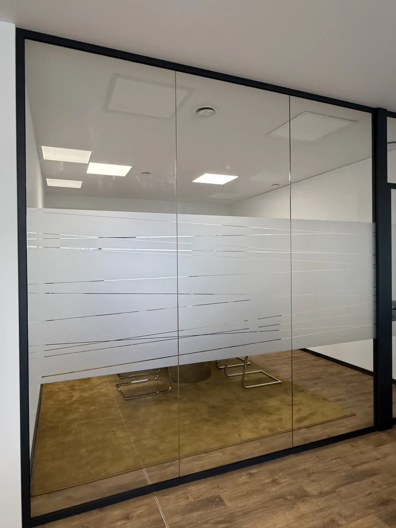 Werbetechnik Dümpel - Augsburg | Glaswand im Büro - gefrostete horizontale Streifen - Besprechungsraum - Reflexion der Deckenleuchten - beiger Teppich - Metallstuhl.